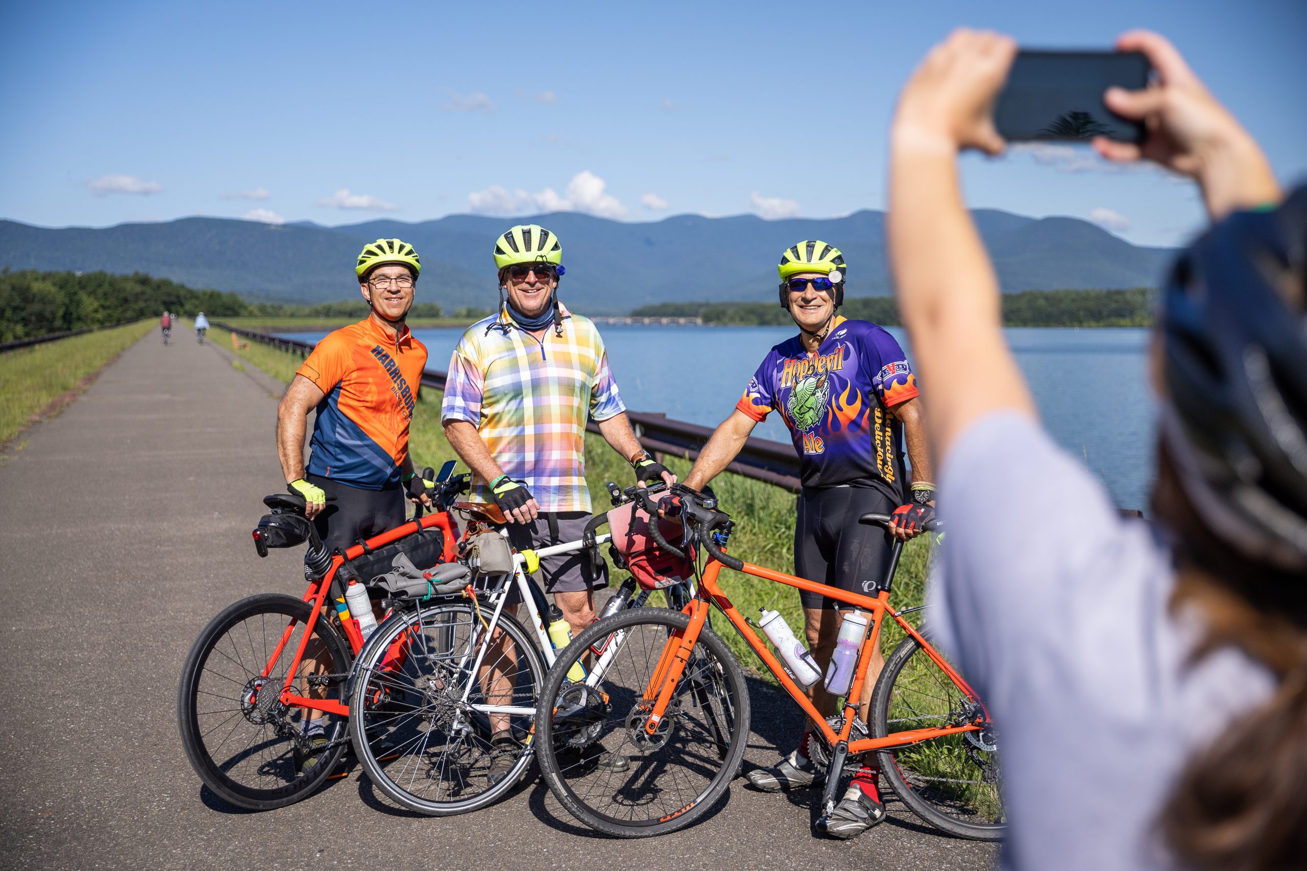 A group of three cyclists pose for a photo on a paved path along the Hudson River.