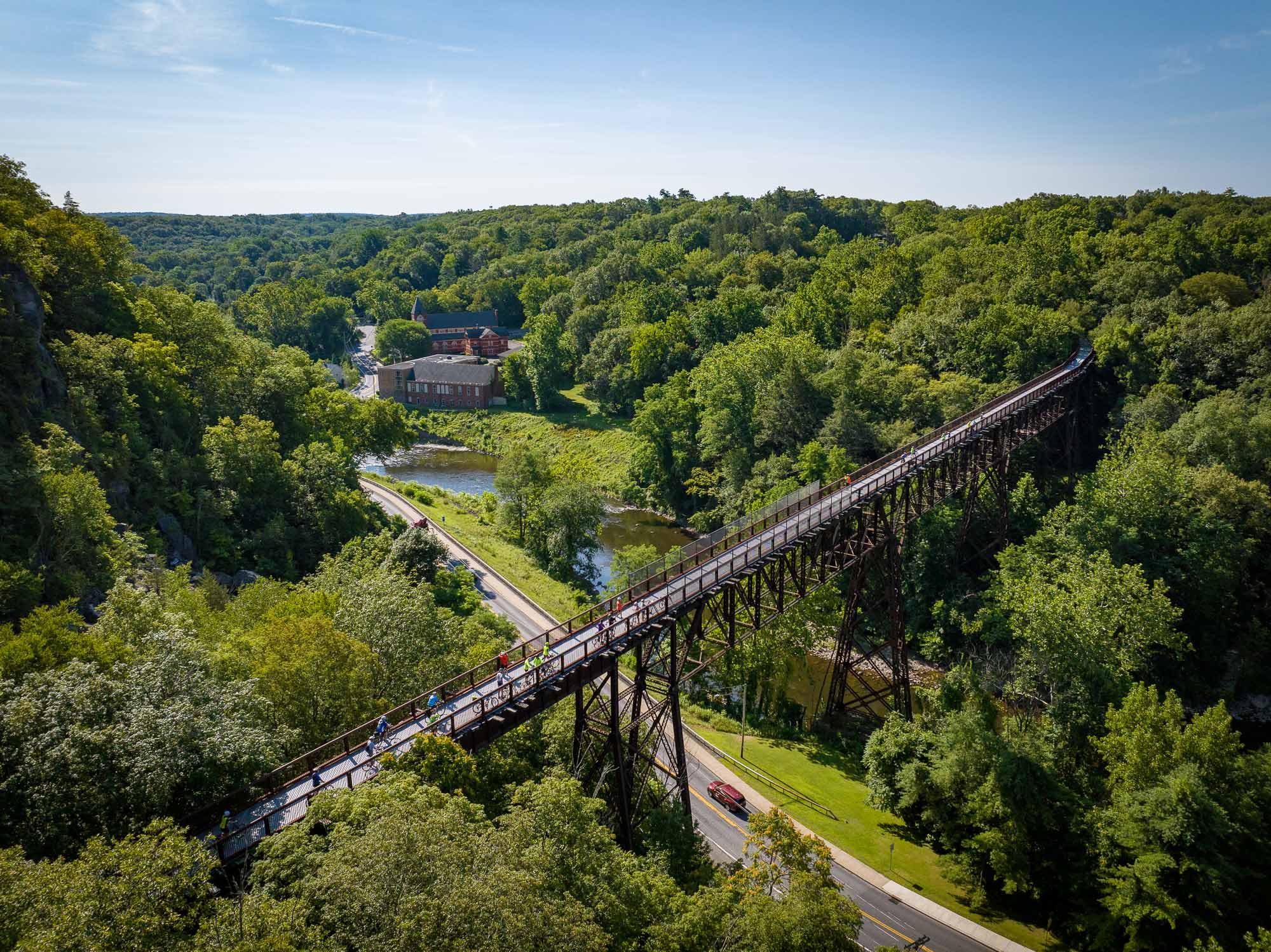 An aerial view of the Rosendale Trestle beside a sea of green trees and bright blue skies.