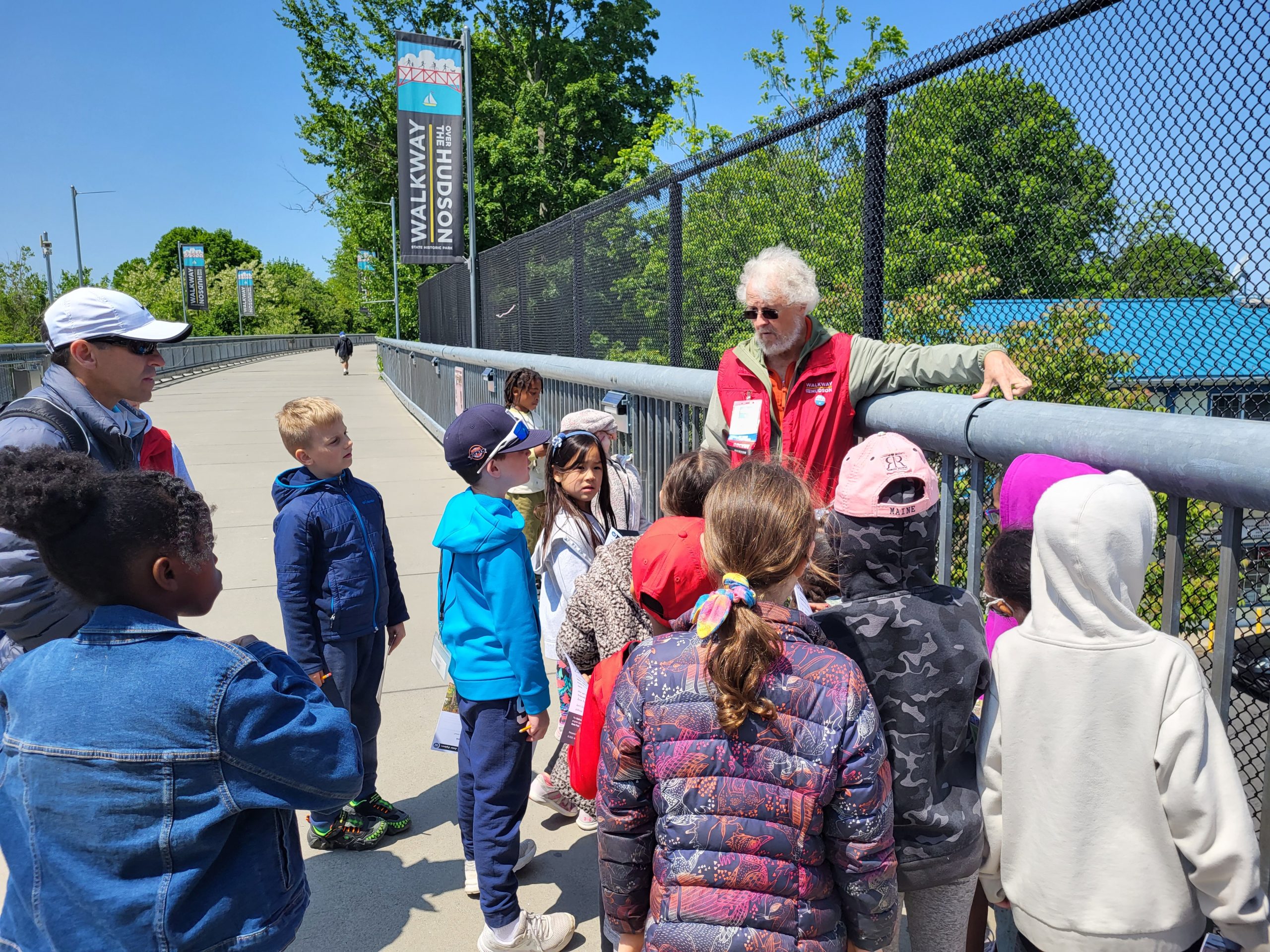 A group of kids stand along a bridge listening to an educator speak.