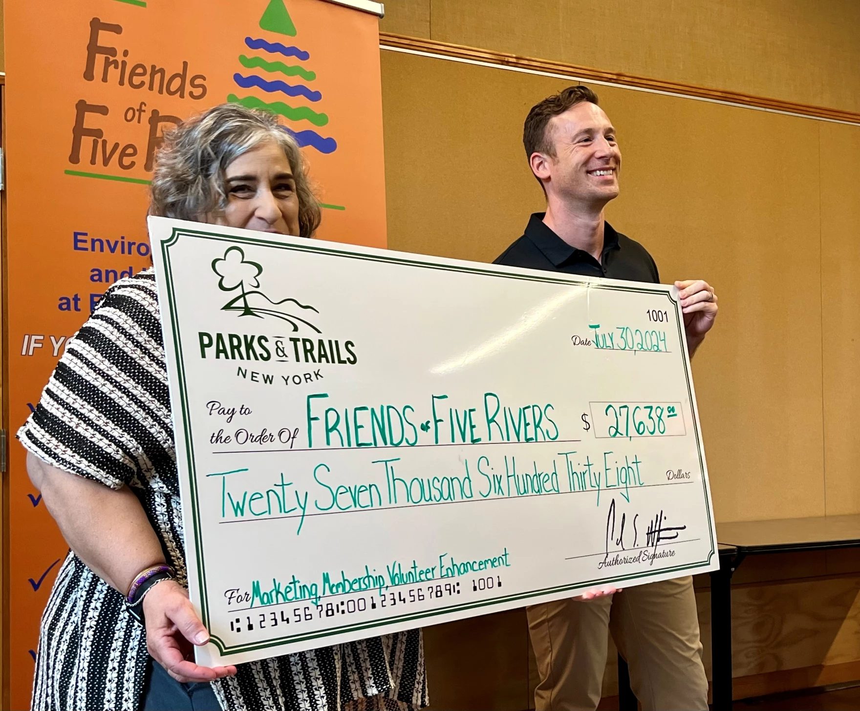 A man and a woman stand alongside one another, holding a big check.