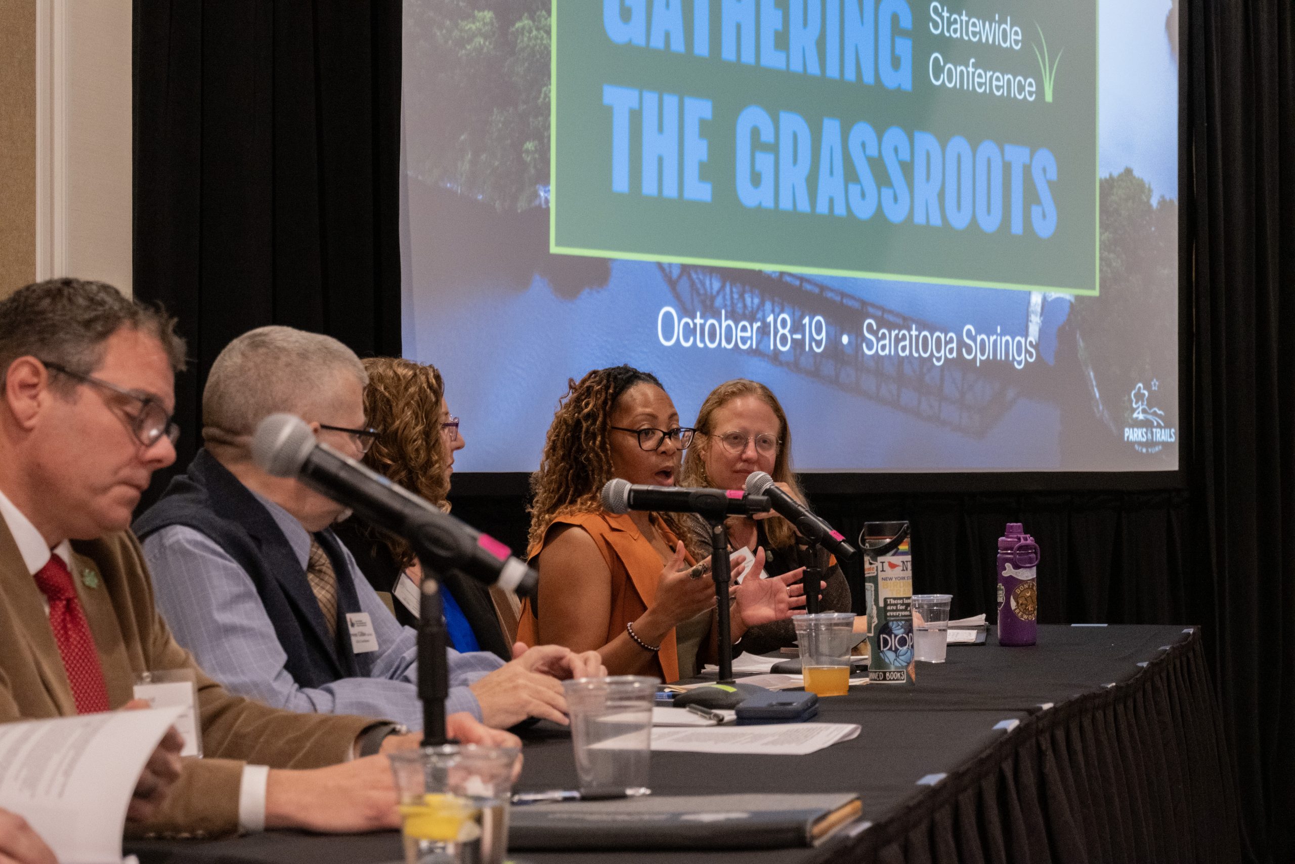 A group of panelists sit along a table, speaking into microphones.