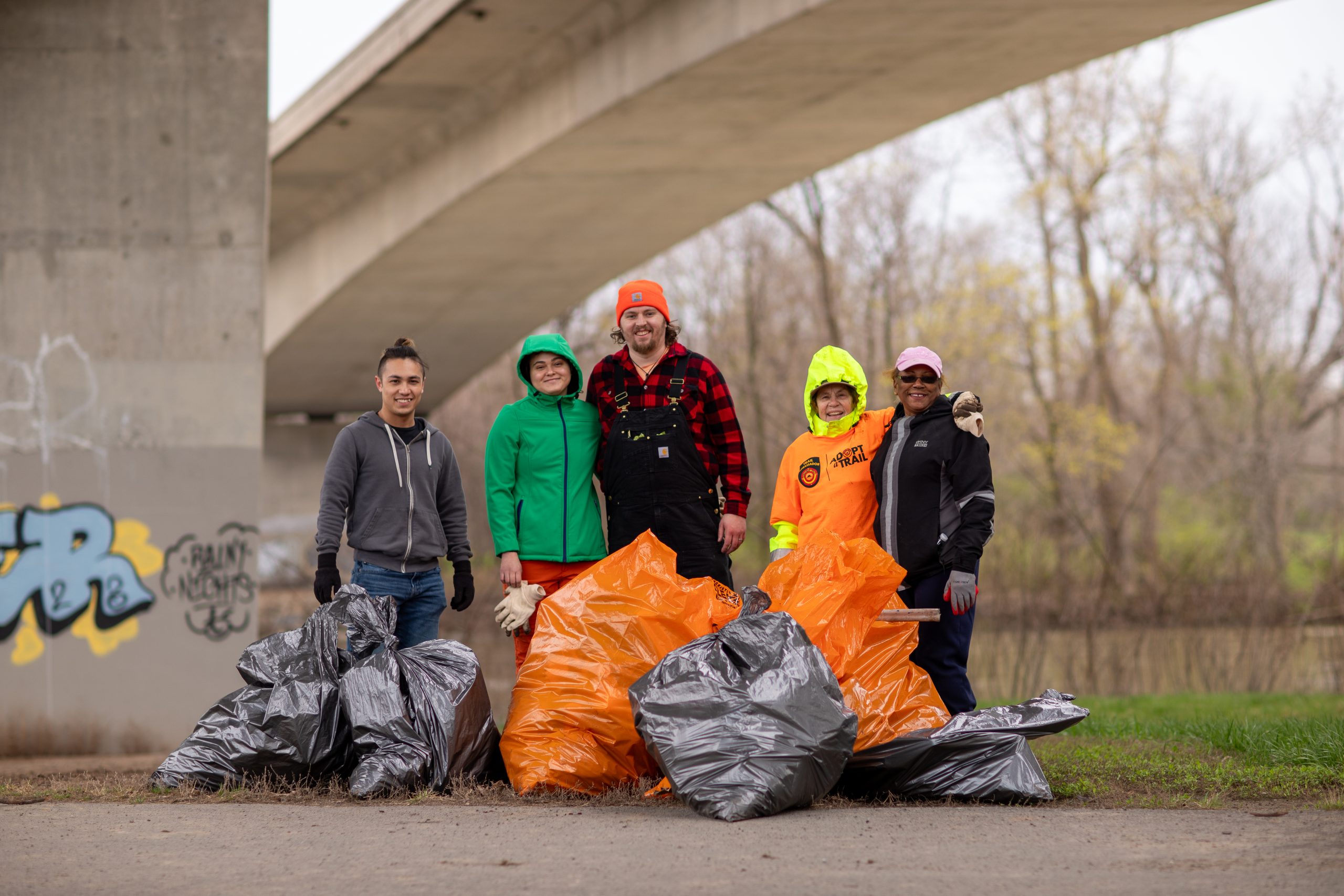 A group of volunteers stand alongside trash bags filled with litter along the Erie Canalway Trail.