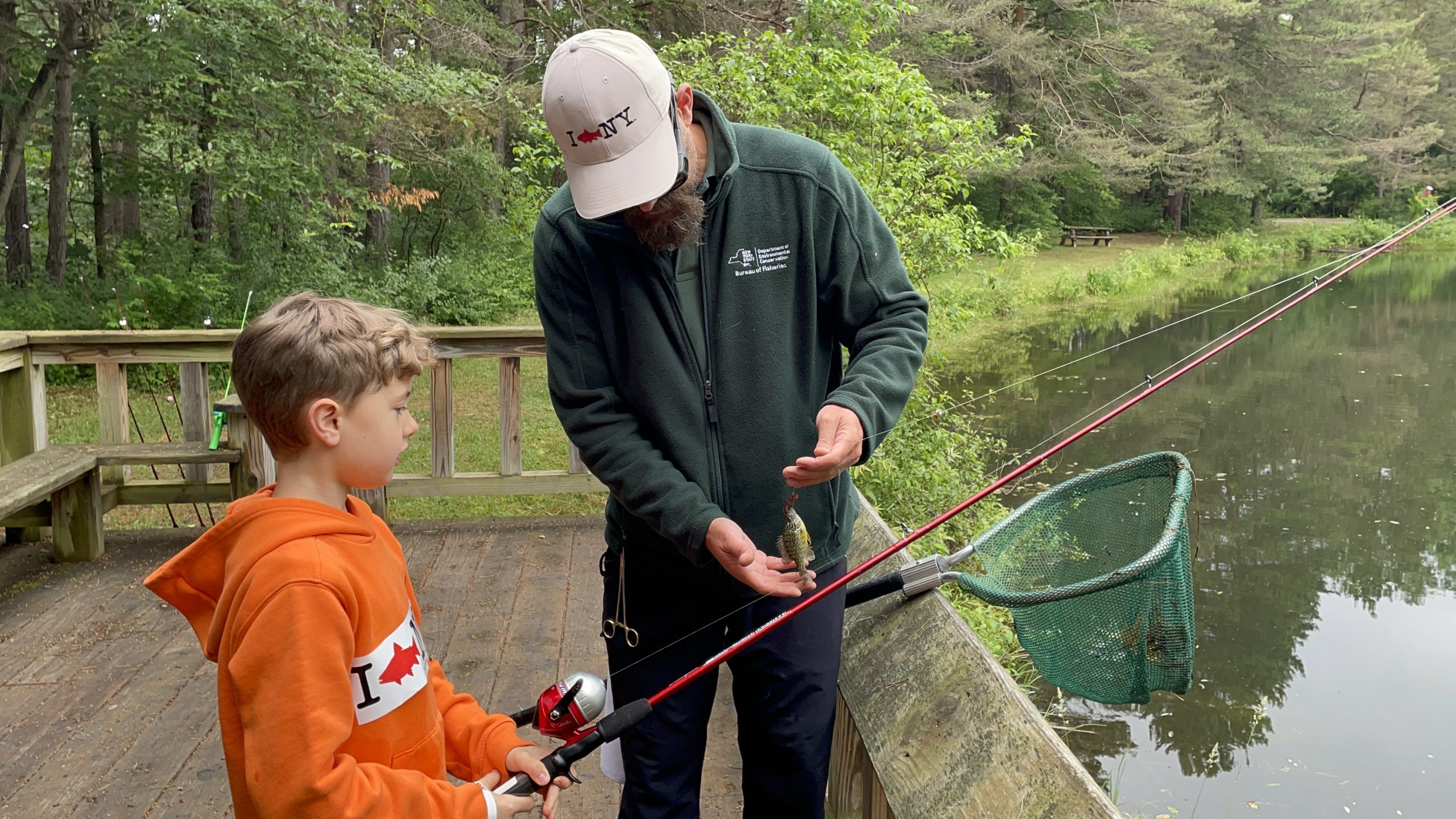 A DEC Staff Member helps a child catch a fish.