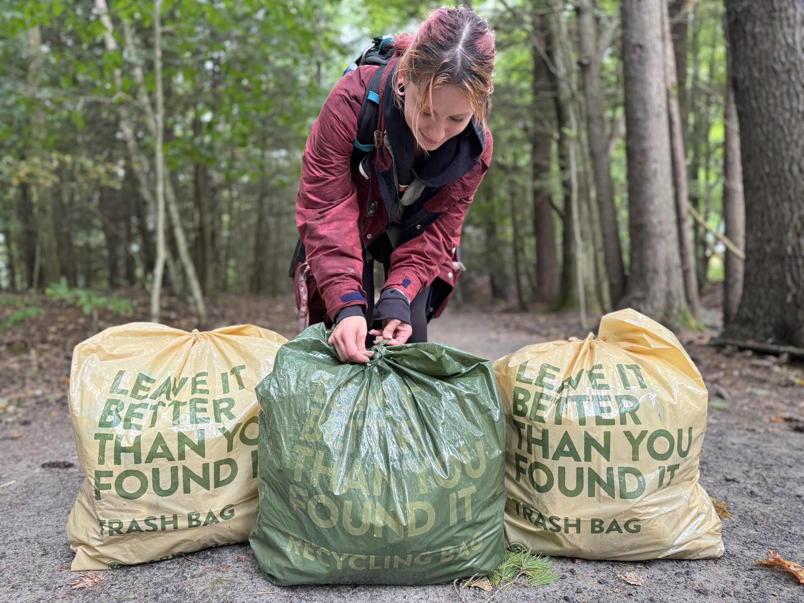 A volunteer ties up a trash bag in the woods.