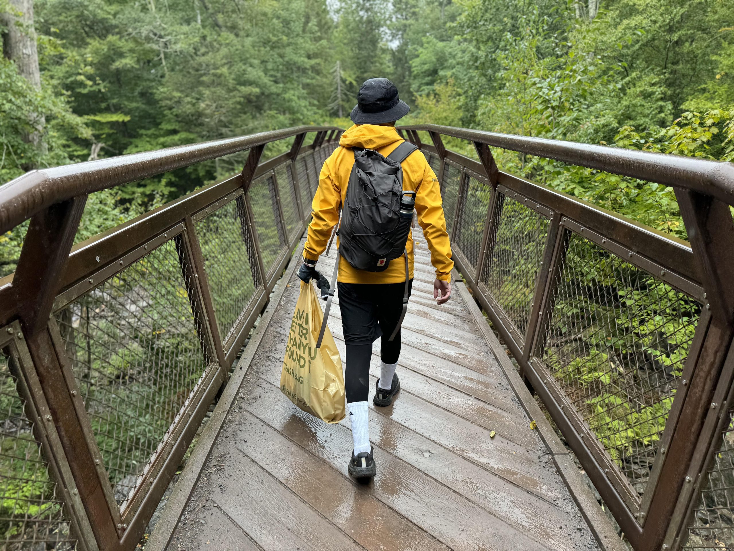 A volunteer holds a trash bag as he walks along a pedestrian bridge.