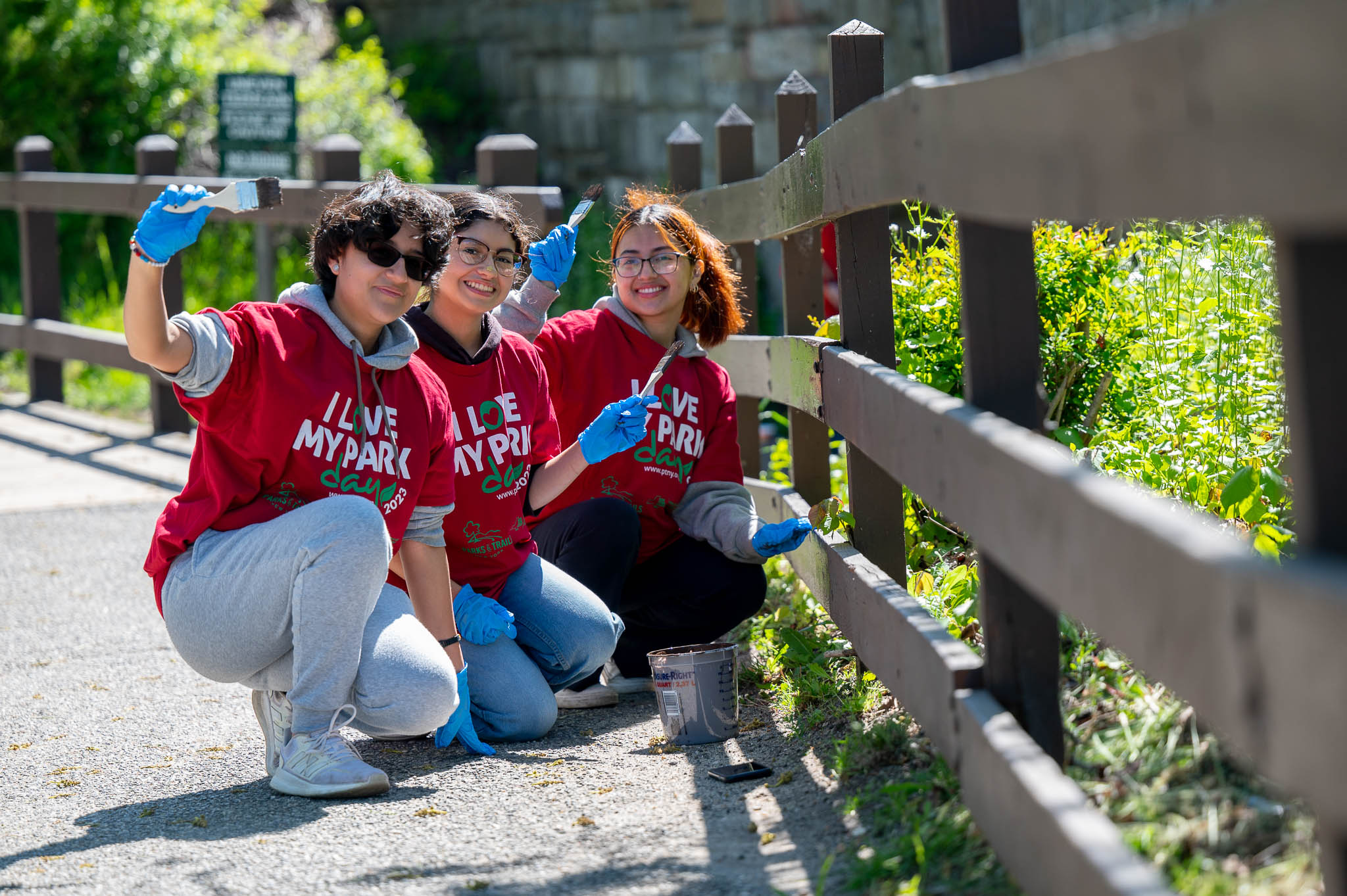 A group of volunteers wave at the camera as they paint a fence.