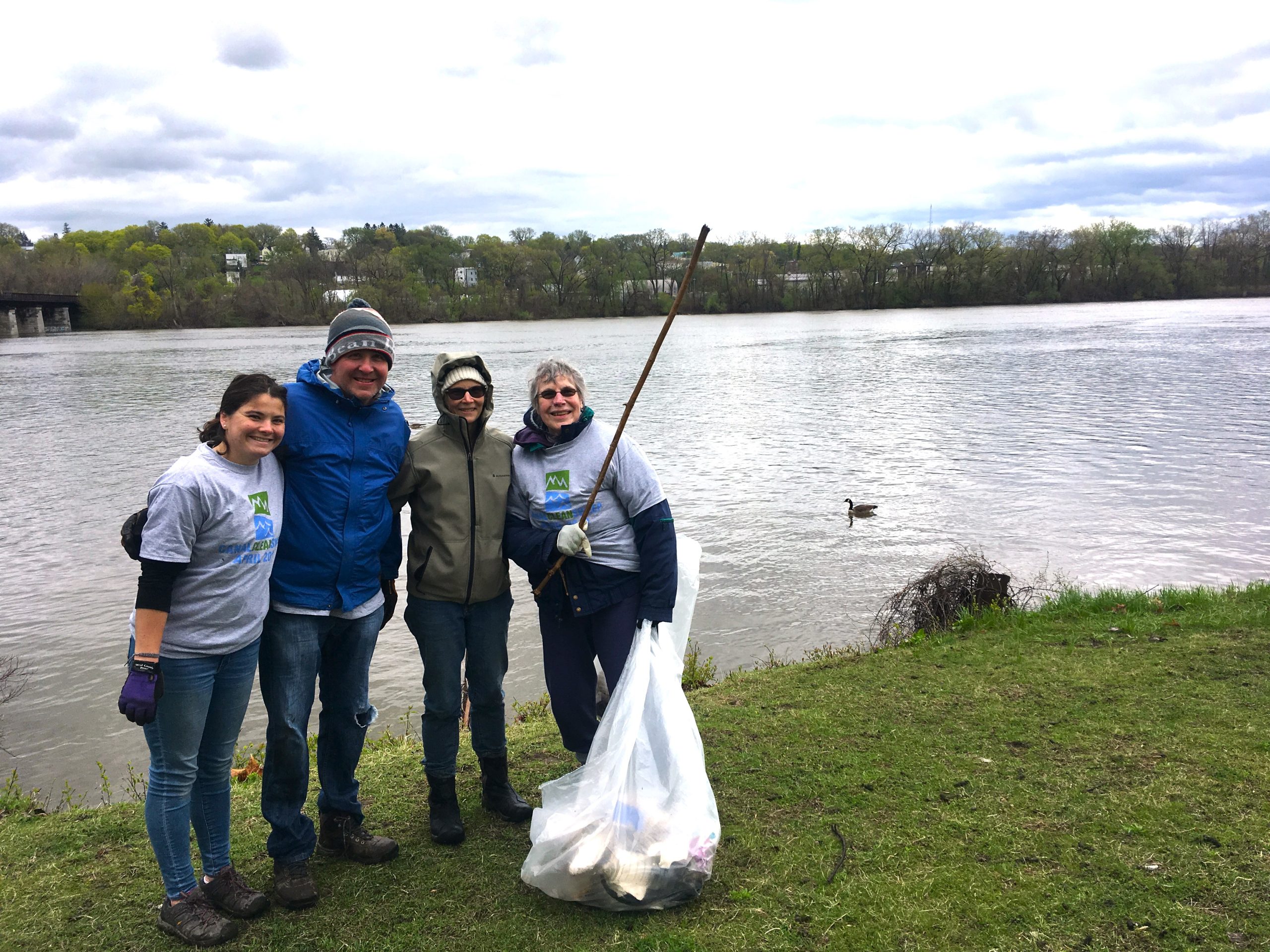 A group of volunteers hold trash bags while picking up litter along the Erie Canal.