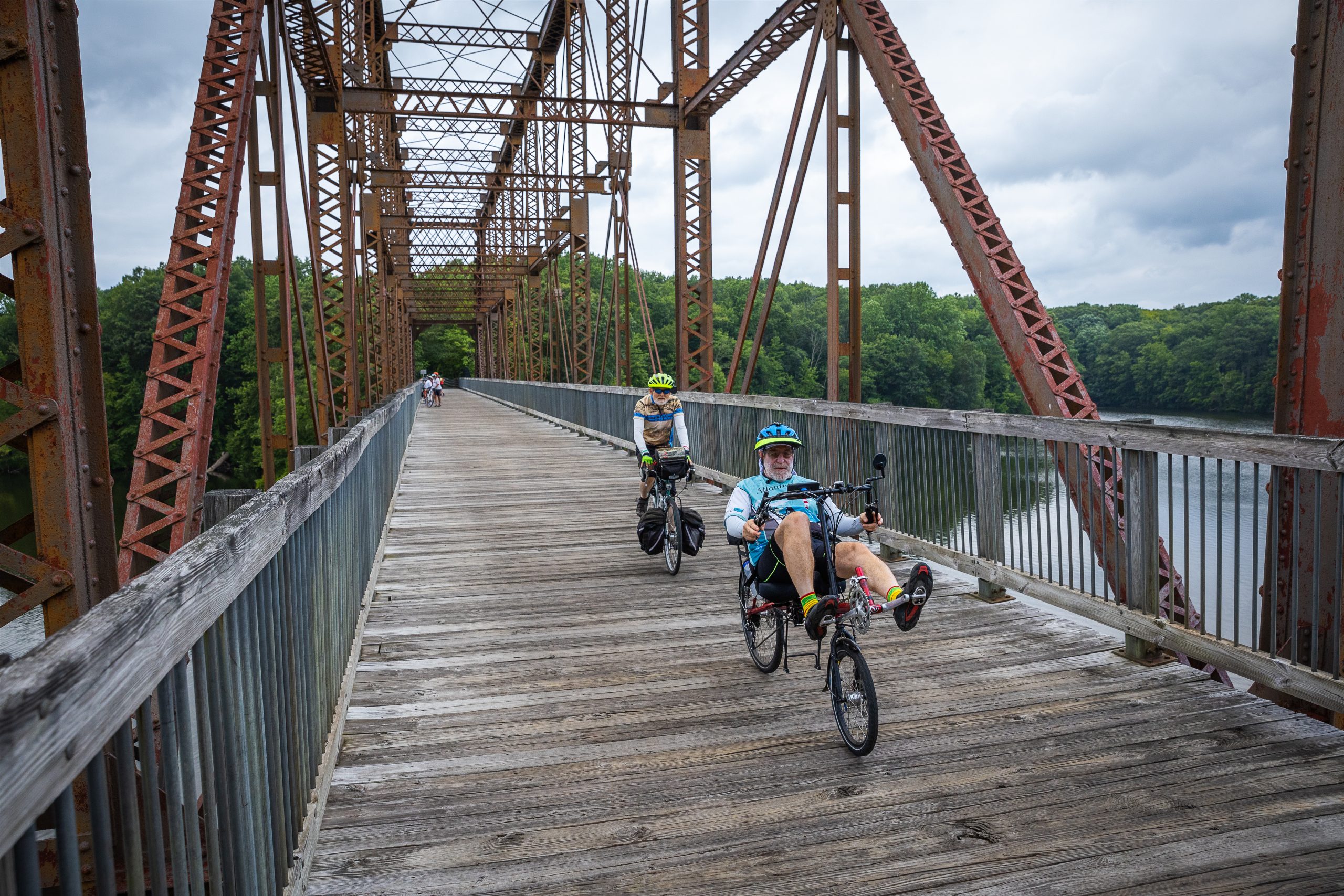 Two cyclists ride along a pedestrian bridge.