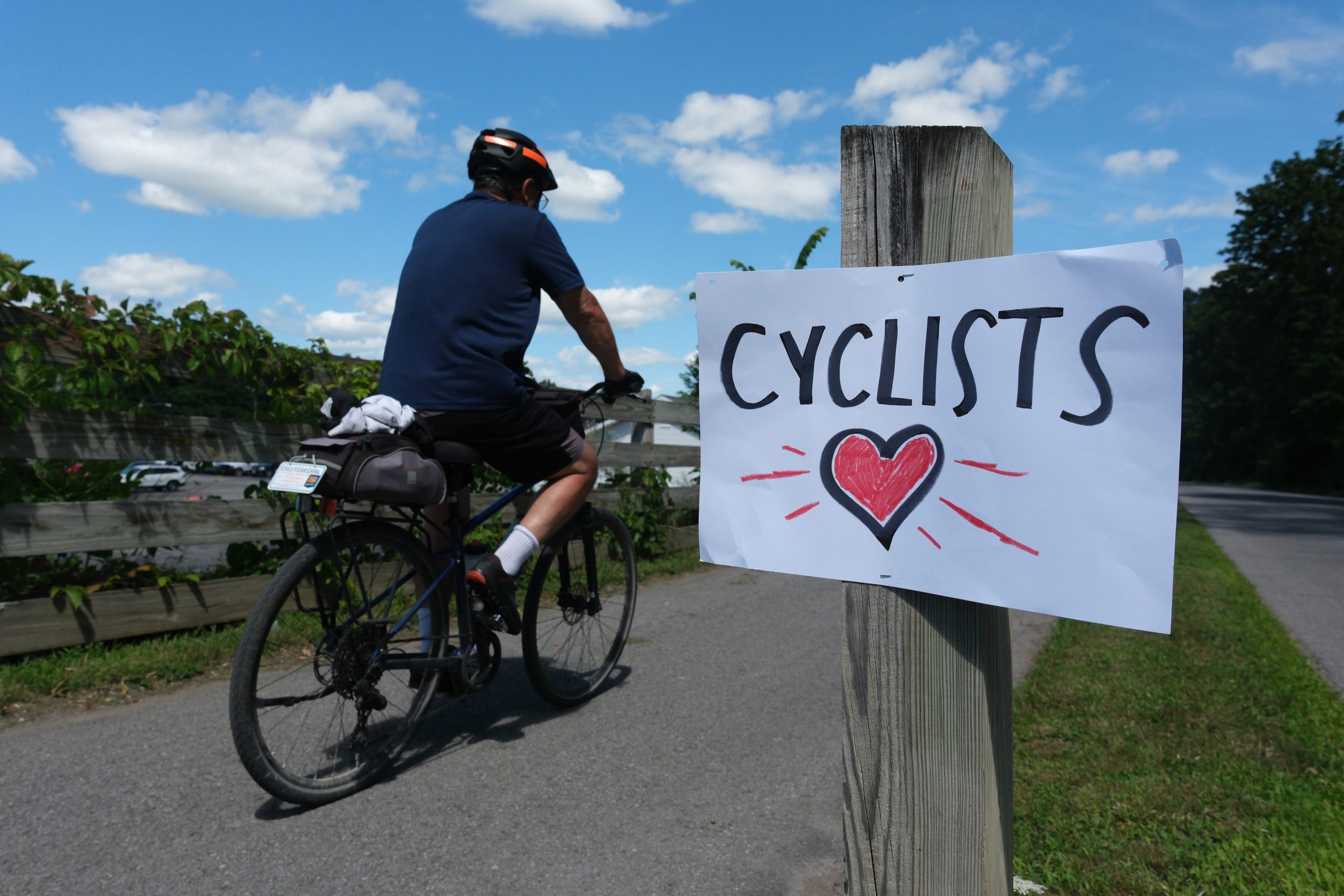 A cyclist rides past a handmade sign with a heart and the word cyclists.