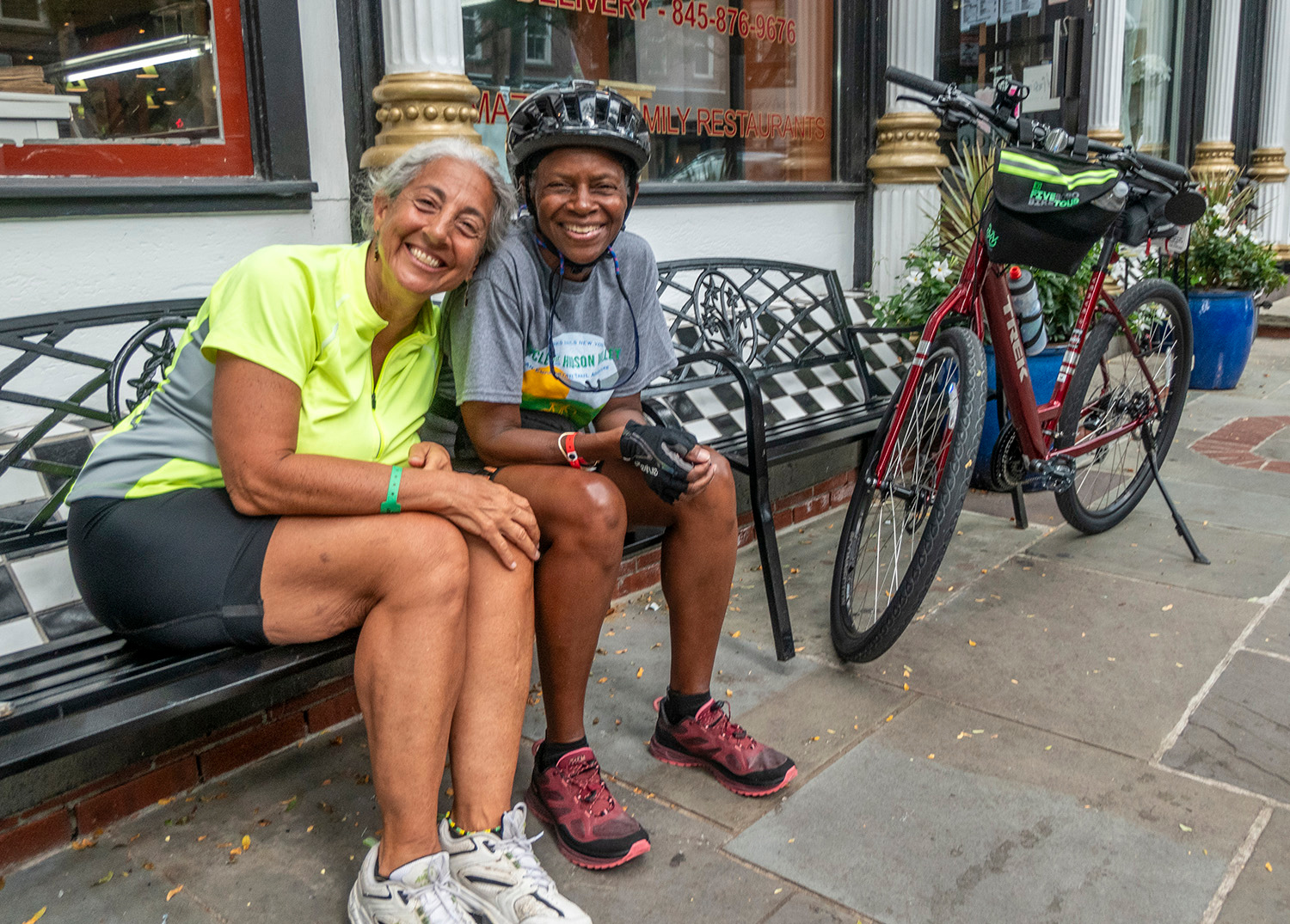 Two women sitting on a bench with their bikes in the background.