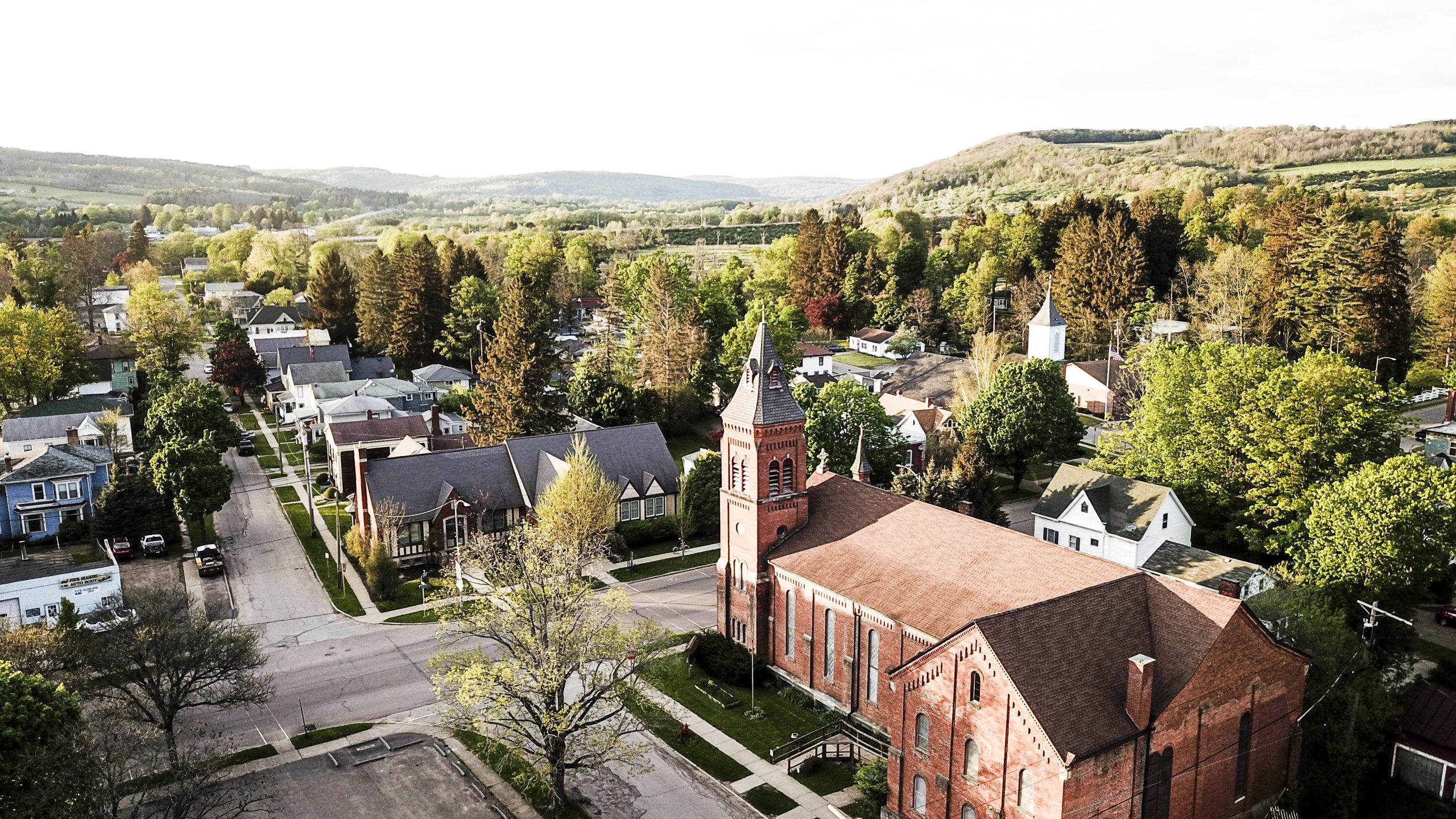 Birds-eye view of the Village of Cuba with green hills in the background and a brick church in the foreground.